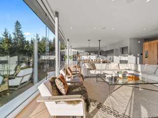 Experience modern luxury in this stunning open-concept living space, featuring floor-to-ceiling windows that bathe the room in natural light and offer breathtaking views of the surrounding forest.