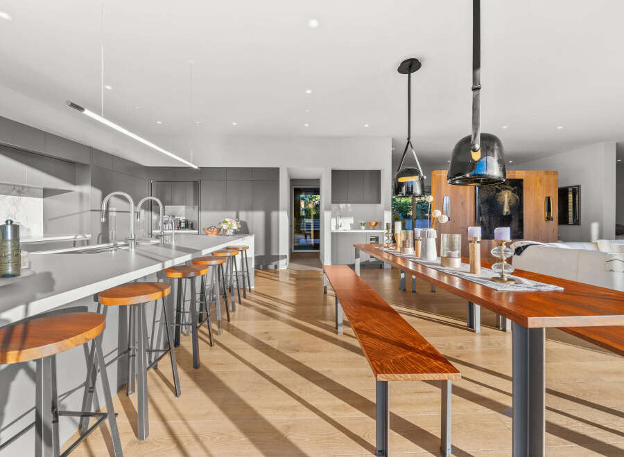 Experience modern luxury in this open-concept kitchen and dining area, featuring a sleek island with bar seating and a spacious wooden dining table perfect for gatherings.