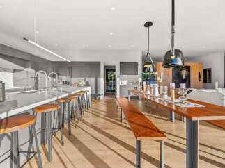 Experience modern luxury in this open-concept kitchen and dining area, featuring a sleek island with bar seating and a spacious wooden dining table perfect for gatherings.