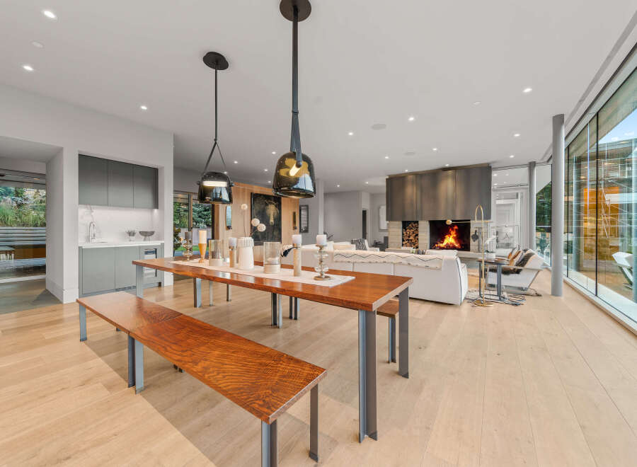 Experience modern luxury in this open-concept living space, featuring a sleek dining area with a long wooden table and benches, perfect for gatherings.