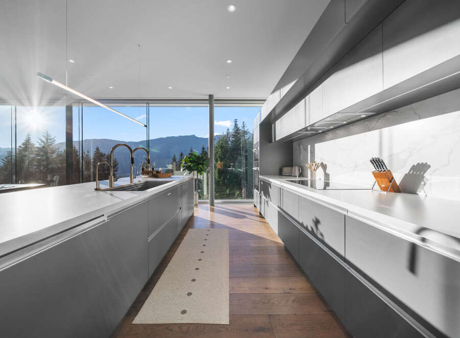 Experience modern luxury in this stunning kitchen featuring sleek grey cabinetry and expansive windows that frame breathtaking mountain and forest views.