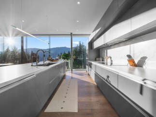 Experience modern luxury in this stunning kitchen featuring sleek grey cabinetry and expansive windows that frame breathtaking mountain and forest views.