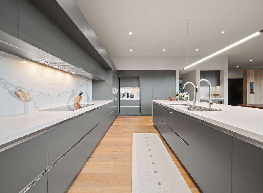 Experience modern luxury in this sleek, gray gourmet kitchen, featuring a stunning marble backsplash and a spacious island with a double sink.