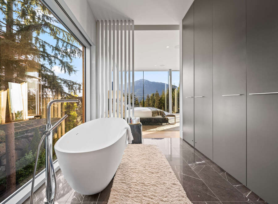 Experience luxury living with this stunning master bathroom featuring a freestanding bathtub and expansive windows offering breathtaking mountain and forest views.
