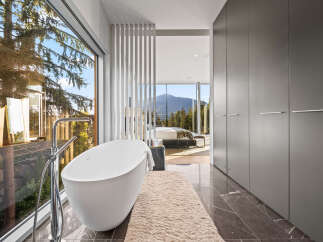 Experience luxury living with this stunning master bathroom featuring a freestanding bathtub and expansive windows offering breathtaking mountain and forest views.