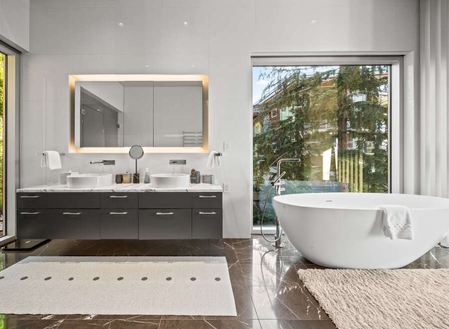 Experience modern luxury in this stunning bathroom featuring a freestanding soaking tub with a sleek chrome faucet and a spacious double vanity with vessel sinks.