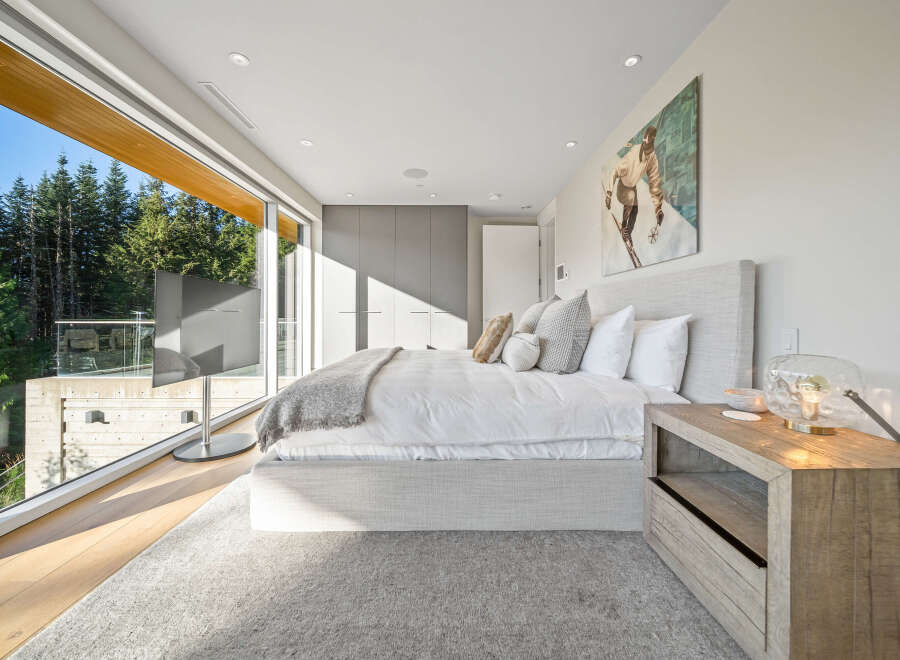 Experience modern luxury in this stunning bedroom featuring a king-sized bed with plush white linens and a cozy throw blanket.