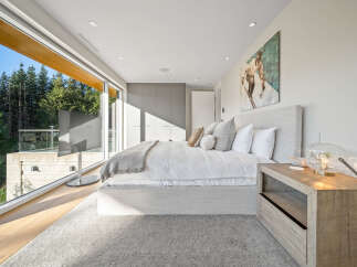 Experience modern luxury in this stunning bedroom featuring a king-sized bed with plush white linens and a cozy throw blanket.