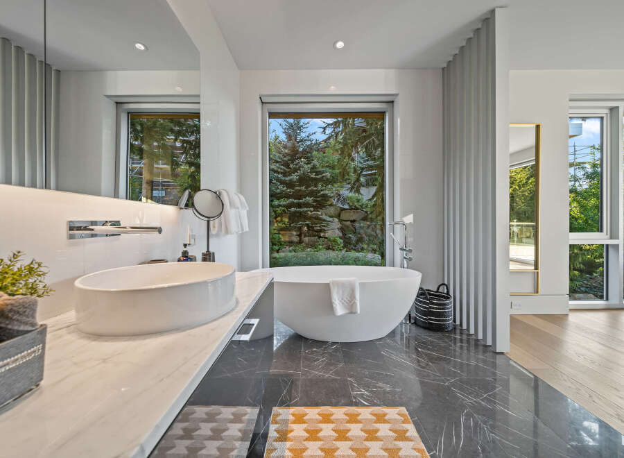 Experience luxury in this stunning modern bathroom featuring a freestanding soaking tub with a breathtaking view of the lush greenery outside.