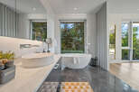 Experience luxury in this stunning modern bathroom featuring a freestanding soaking tub with a breathtaking view of the lush greenery outside.