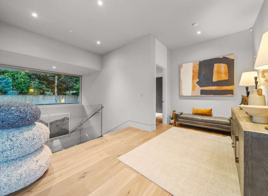 This modern hallway features a large window overlooking lush greenery, a stylish leather bench with a mustard accent pillow, and a striking abstract art piece.