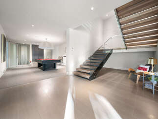 Experience modern living in this spacious recreational area featuring a sleek pool table and a stunning floating staircase with glass railings.