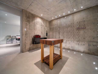 Discover a unique wine cellar with a rustic concrete aesthetic, featuring a prominent butcher block table as a centerpiece.
