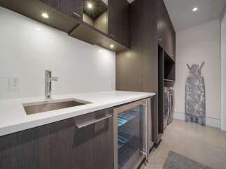 This modern laundry room features a sleek white countertop with an undermount sink and a chrome faucet, complemented by dark wood cabinetry.