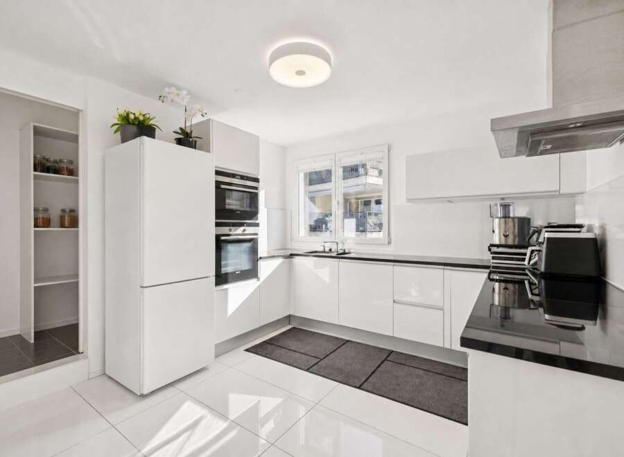 Experience modern living in this sleek, white kitchen featuring integrated stainless steel appliances, including double ovens and a built-in refrigerator.