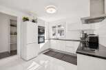 Experience modern living in this sleek, white kitchen featuring integrated stainless steel appliances, including double ovens and a built-in refrigerator.