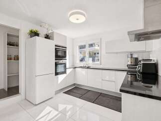 Experience modern living in this sleek, white kitchen featuring integrated stainless steel appliances, including double ovens and a built-in refrigerator.