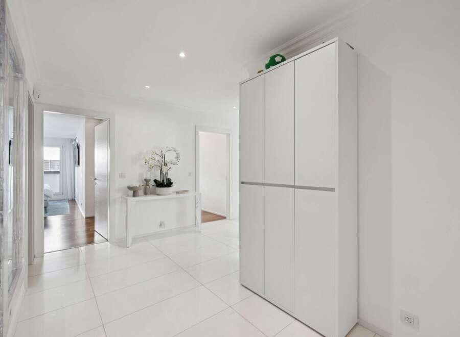 Step into this bright and airy hallway, featuring pristine white tiled floors that reflect the abundant natural light.