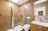 This modern bathroom features a sleek design with warm brown tiled walls and a spacious walk-in shower enclosed by a glass panel and a light-colored curtain.