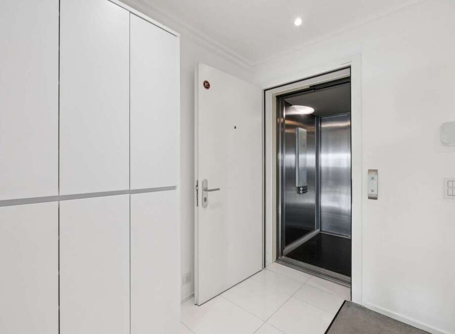 Step into modern convenience with this spacious entryway featuring a sleek white wardrobe and direct access to a private elevator.