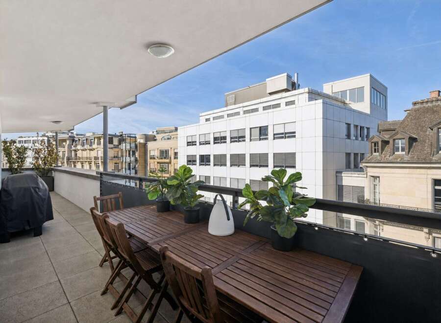 Enjoy outdoor living on this spacious balcony, perfect for al fresco dining with a large wooden table and chairs.