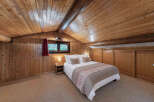 Experience rustic charm in this cozy attic bedroom, featuring warm wood paneling and a sloped ceiling with exposed beams.