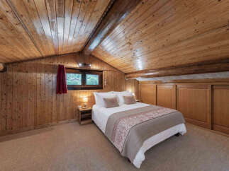 Experience rustic charm in this cozy attic bedroom, featuring warm wood paneling and a sloped ceiling with exposed beams.