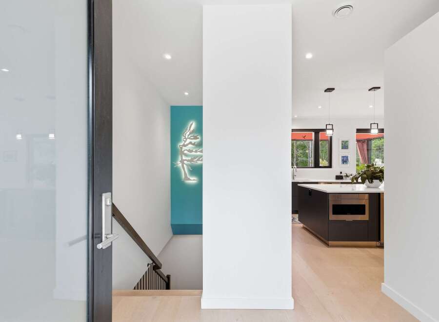 Step into a modern oasis with this stunning property, featuring a sleek entryway with a glass door and a striking tree-shaped wall art.