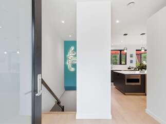 Step into a modern oasis with this stunning property, featuring a sleek entryway with a glass door and a striking tree-shaped wall art.