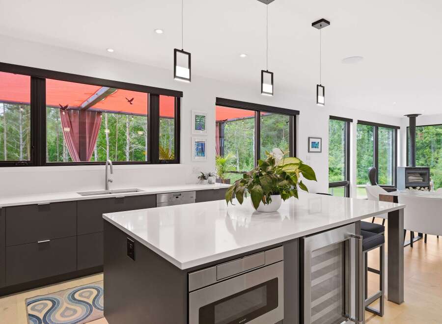 Experience modern living in this stunning kitchen featuring sleek dark cabinetry, a spacious white quartz island with integrated appliances, and a wine fridge.