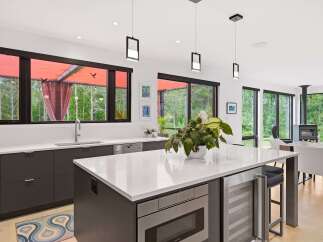 Experience modern living in this stunning kitchen featuring sleek dark cabinetry, a spacious white quartz island with integrated appliances, and a wine fridge.