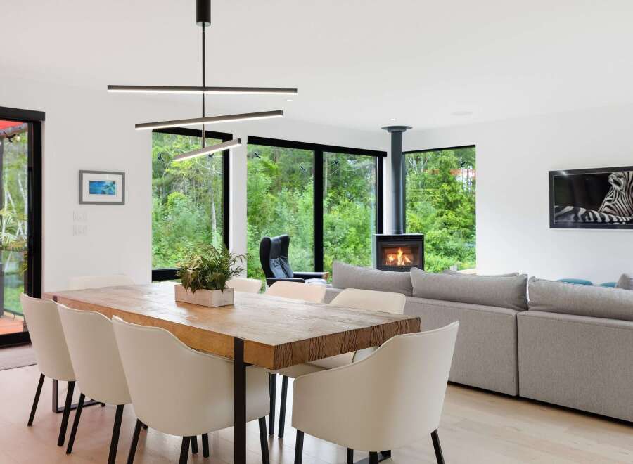 Experience modern living in this stunning open-concept space, featuring a large wooden dining table perfect for gatherings and a cozy living area with a contemporary fireplace.