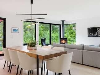 Experience modern living in this stunning open-concept space, featuring a large wooden dining table perfect for gatherings and a cozy living area with a contemporary fireplace.