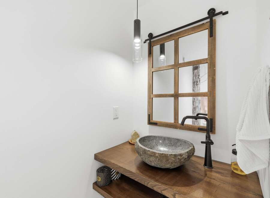 This modern bathroom features a unique stone vessel sink atop a rustic live-edge wood vanity.