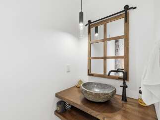 This modern bathroom features a unique stone vessel sink atop a rustic live-edge wood vanity.