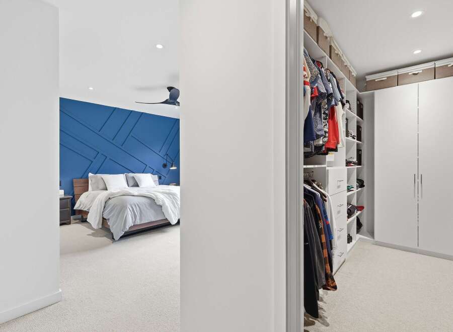 Step into a luxurious master suite featuring a striking blue accent wall with a geometric design, complemented by a plush carpet and a modern ceiling fan.