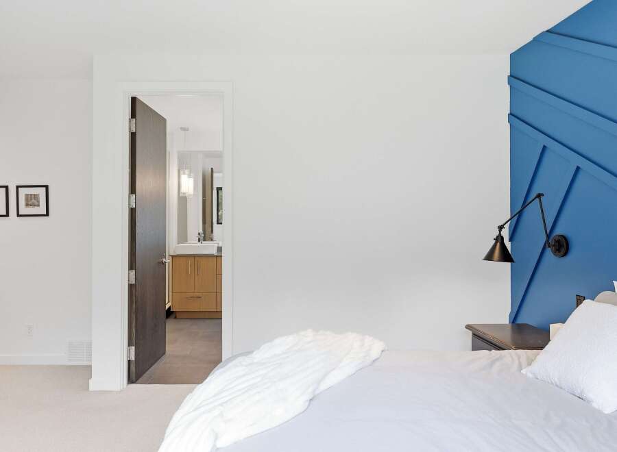 Experience modern comfort in this inviting bedroom, featuring a striking blue accent wall with a geometric design and a sleek, adjustable wall lamp.