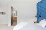 Experience modern comfort in this inviting bedroom, featuring a striking blue accent wall with a geometric design and a sleek, adjustable wall lamp.