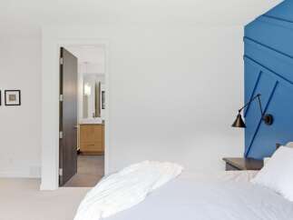 Experience modern comfort in this inviting bedroom, featuring a striking blue accent wall with a geometric design and a sleek, adjustable wall lamp.