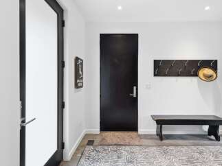 Step into this modern entryway featuring a sleek black door and a convenient coat rack with a stylish straw hat.
