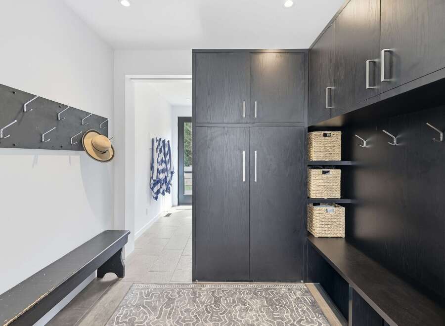 This modern entryway features a sleek dark wood built-in cabinet system with ample storage and convenient hooks for coats and accessories.