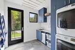 This modern laundry room features sleek navy blue cabinetry, a stainless steel sink, and a stacked Maytag washer and dryer.