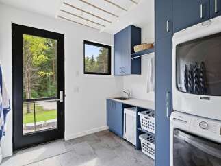 This modern laundry room features sleek navy blue cabinetry, a stainless steel sink, and a stacked Maytag washer and dryer.