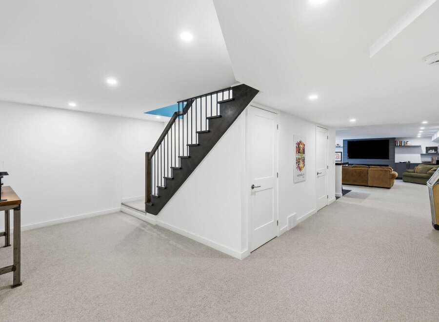 Discover this beautifully finished basement featuring a modern staircase with black railings and a bright, open-concept living area.