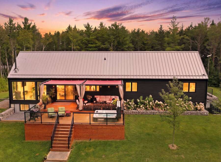 Experience modern living in this stunning home featuring a spacious wooden deck with a relaxing hot tub and comfortable outdoor seating.