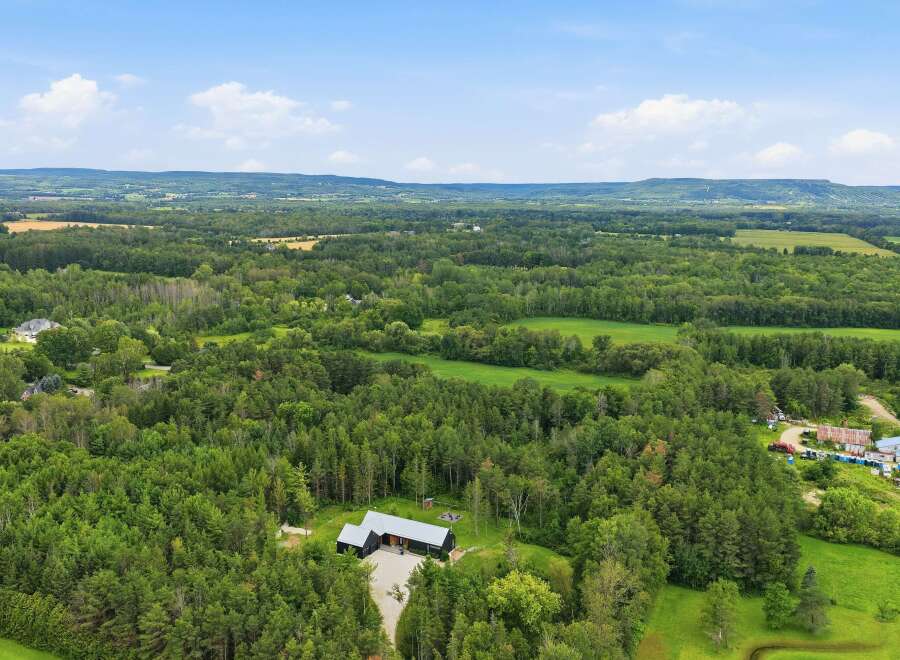 Discover this stunning property featuring a modern dark-colored home nestled amidst lush greenery and mature trees.