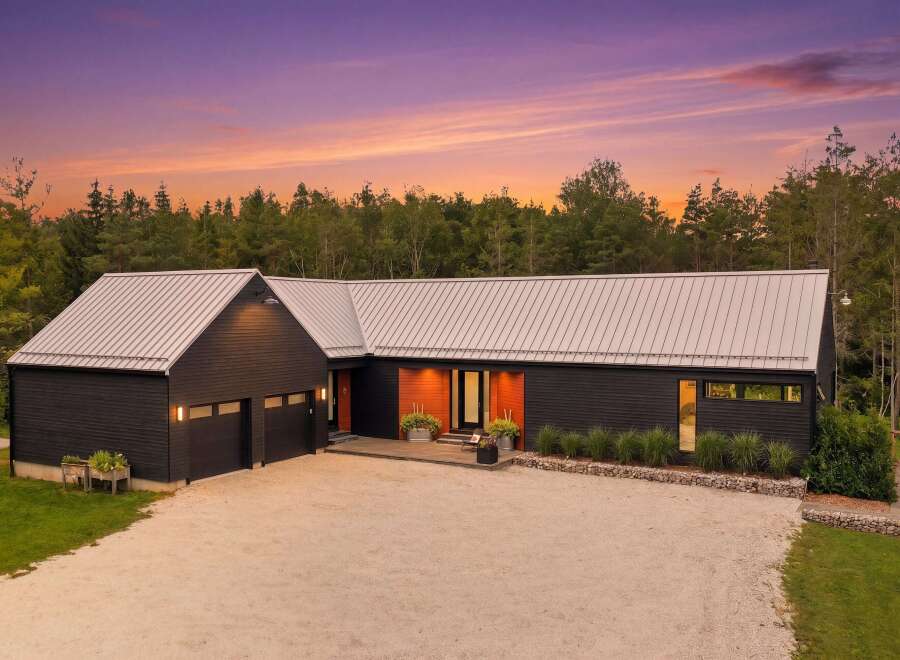Experience modern living in this stunning dark-clad home, featuring a sleek metal roof and a striking wood-accented entrance.