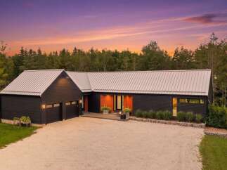 Experience modern living in this stunning dark-clad home, featuring a sleek metal roof and a striking wood-accented entrance.