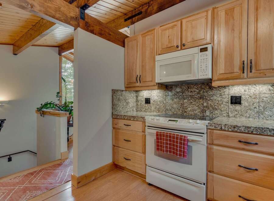 Discover a charming kitchen featuring light wood cabinetry and a built-in microwave, complemented by granite countertops and a tiled backsplash.