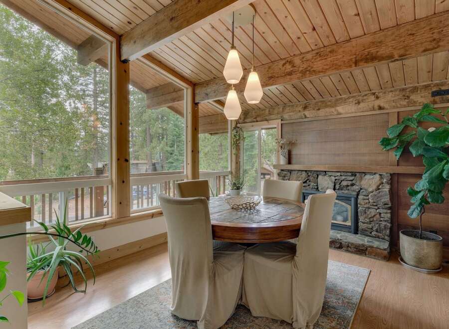 Experience cozy dining with a view in this charming space, featuring a rustic round dining table and chairs set against a backdrop of large windows overlooking a serene forest.
